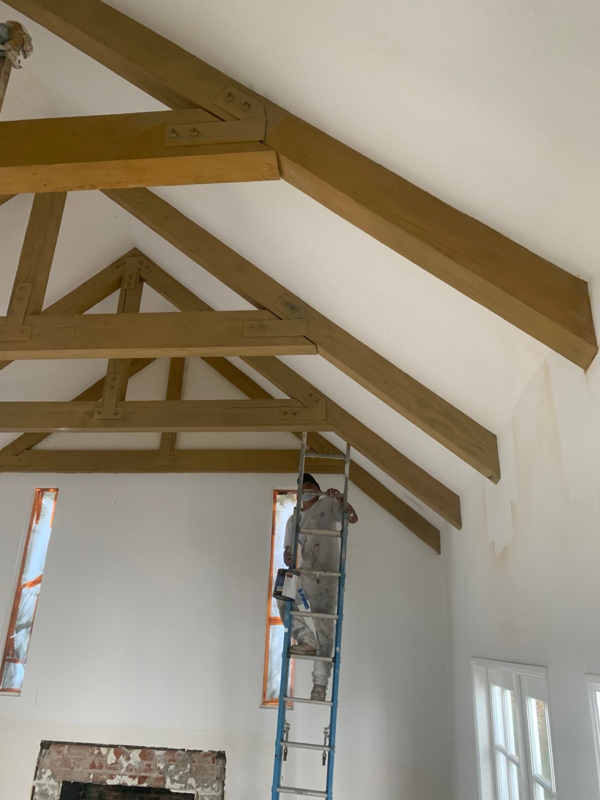 FirstPro painter on a ladder cutting in along a vaulted ceiling with exposed beams
