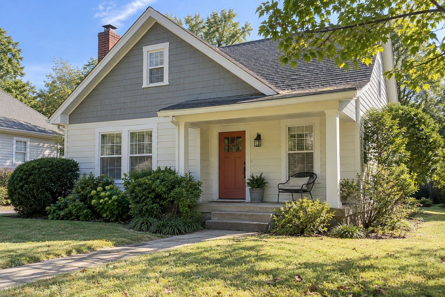 Cottage-style home with cream siding, gray shingle gable and an orange front door